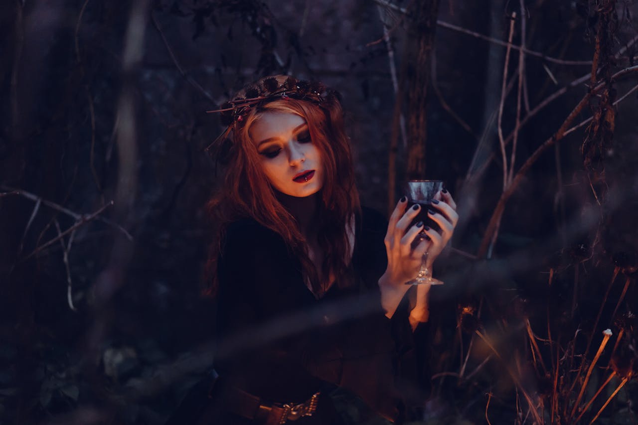 Services A mystical woman in gothic attire holds a chalice amidst a dark, eerie forest setting.