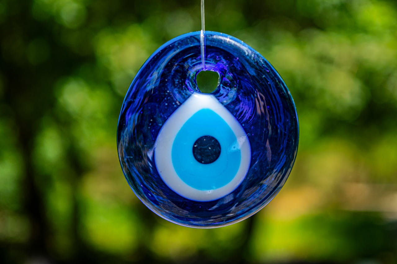 Close-up of a blue evil eye glass pendant hanging outdoors, symbolizing protection.